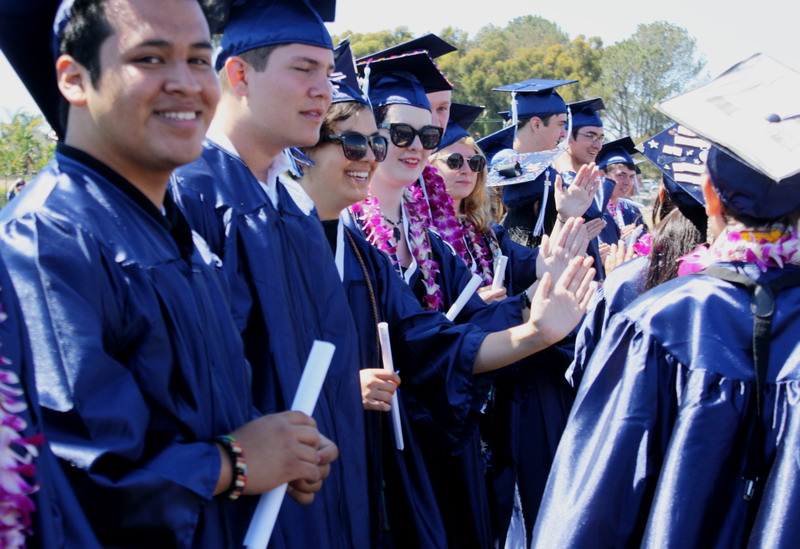 Students give their classmates high fives as they return to their seats after walking down the aisle. high-five