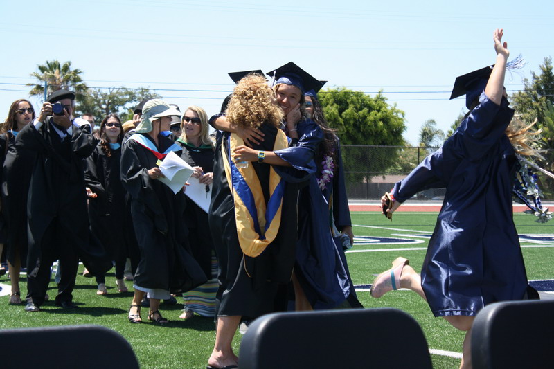 Assistant Jeanne Jones gives the graduating seniors "good bye" hugs as they walk to their seats. hugs