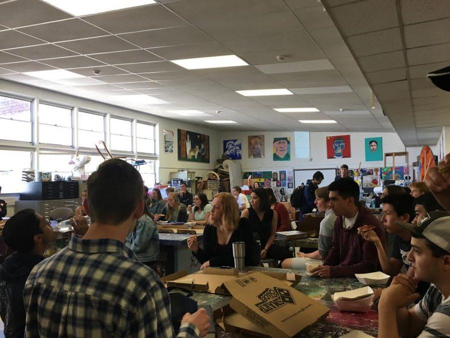 Students eat pizza in the art room during the Forum.