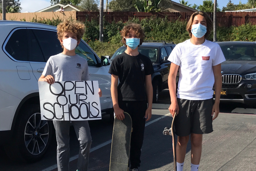 Skateboarders ride around the district office holding signs to open schools 