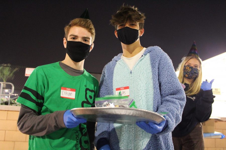 Juniors Ethan Fitzgerald (left) Lucas Casazza (middle) and sophomore Maisie Leeuw (right) pass out candy bags in the front parking lot for students to enjoy