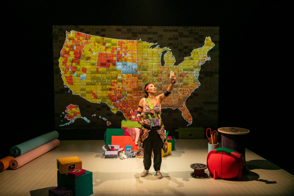Kristina Wong, a Chinese-American woman, stands center, holding her phone in front of a projected map of the US.
